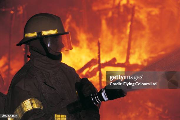 side view of a firefighter holding a fire hose putting out a fire - in flames i the mask stock pictures, royalty-free photos & images