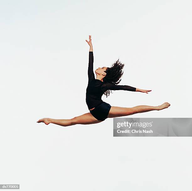 ballet dancer doing the splits in mid air with one arm raised - split acrobatiek stockfoto's en -beelden