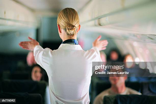 rear view of air stewardess explaining aeroplane safety to passengers - tripulación fotografías e imágenes de stock