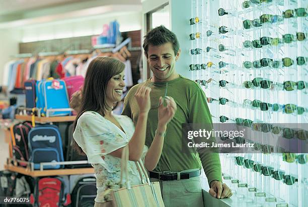 hispanic couple looking at sunglasses in an airport's duty free shop - duty free photos et images de collection