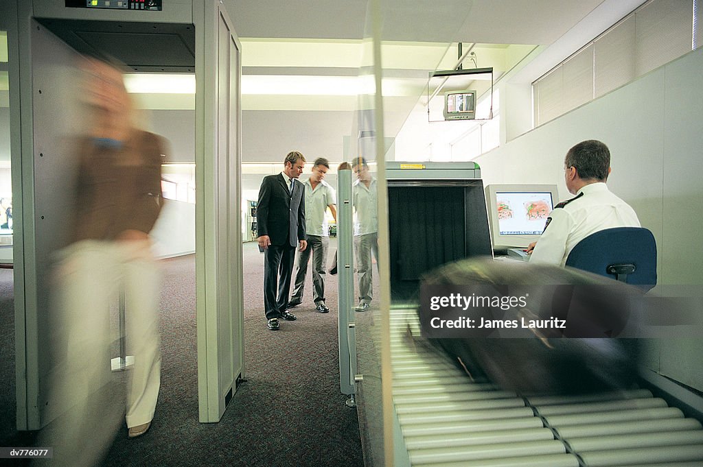 Woman Walking Through a Metal Detector as Her Baggage is X-Rayed at the Airport