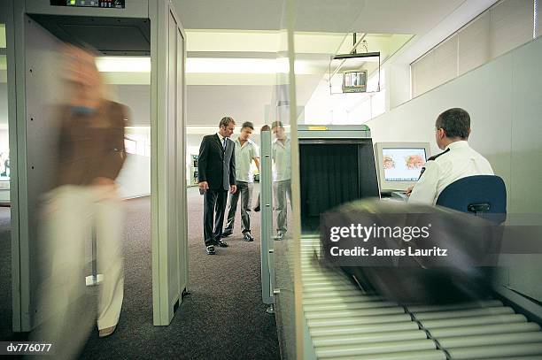 woman walking through a metal detector as her baggage is x-rayed at the airport - customs agent stock pictures, royalty-free photos & images