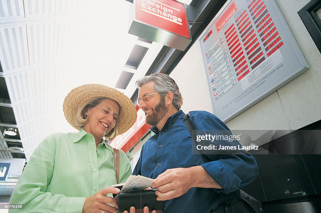 Couple Standing by a Bureau de Change at an Airport