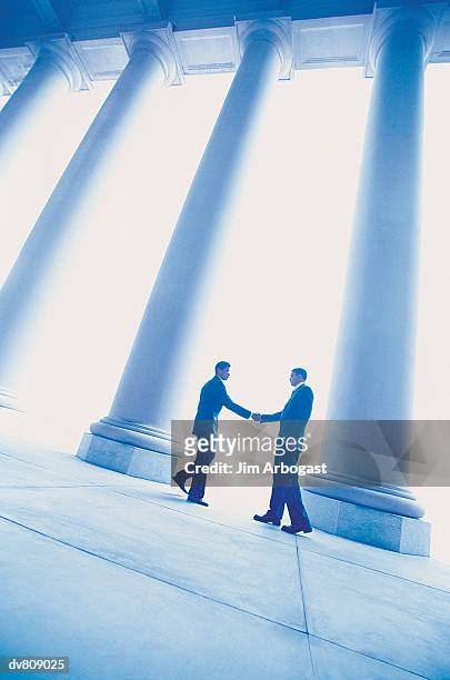 two businessmen shaking hands in front of a row of columns - premiere of front row filmed entertainments the pirates of somalia red carpet stockfoto's en -beelden