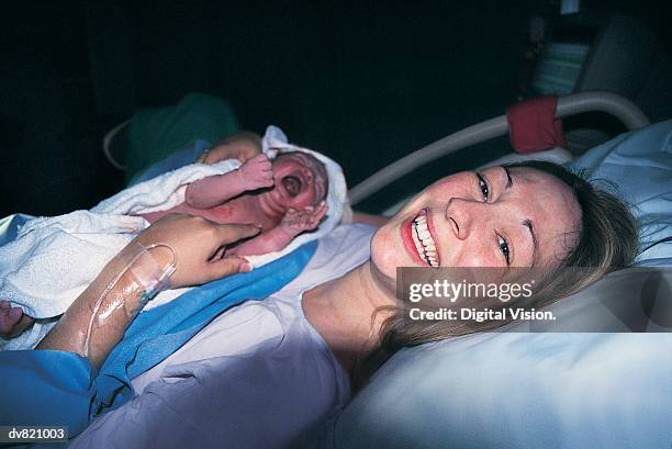 woman smiling holding her newborn baby - moms crying in bed stockfoto's en -beelden
