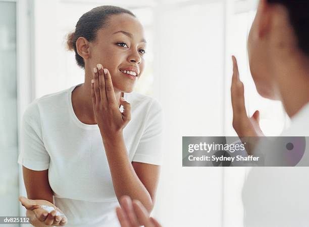 woman applying moisturizer - bathroom mirror fotografías e imágenes de stock