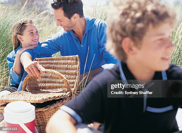 father and daughter by a picnic hamper behind a young boy on the dunes - sydney fotografías e imágenes de stock