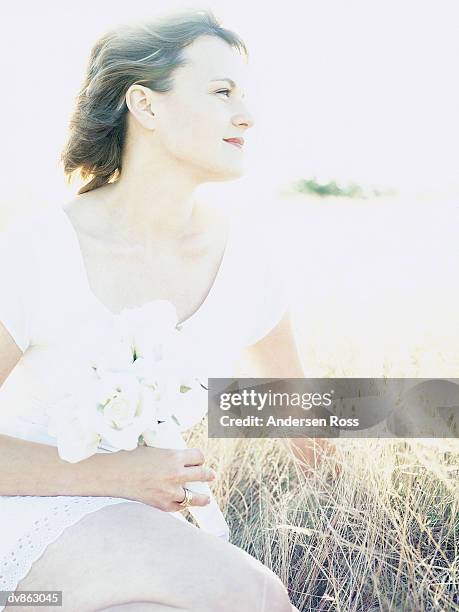 portrait of a woman sitting in a field holding a bunch of flowers - ross stockfoto's en -beelden