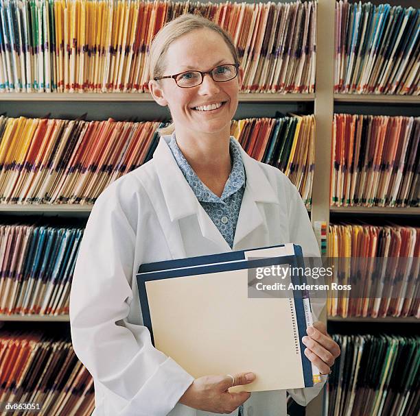 portrait of a doctor holding a file and standing in front of rows of filing - ross stockfoto's en -beelden