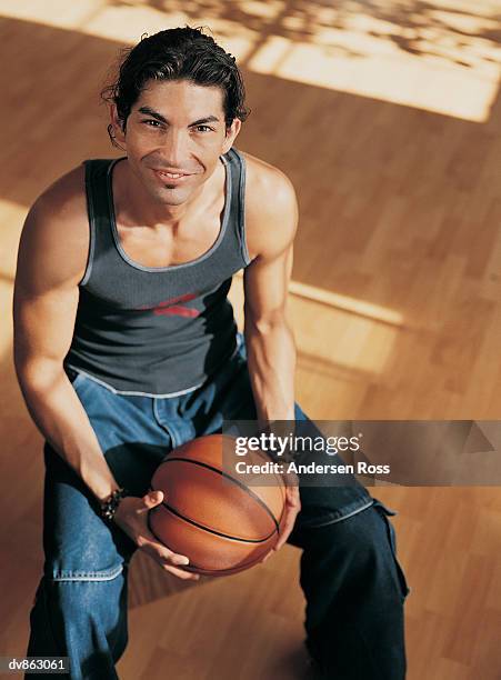 portrait of a young man sitting in a gym and holding a basketball - a ross stock-fotos und bilder