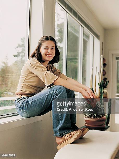 portrait of a female teenager sitting on a window sill - andersen ross stock pictures, royalty-free photos & images