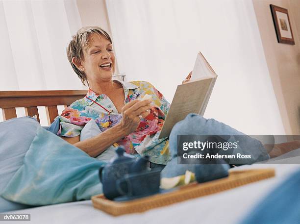 mature woman reading a book in bed - a ross stock-fotos und bilder