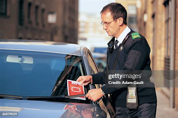 traffic warden attaching a parking ticket to a car's windscreen - verkeerspolitie stockfoto's en -beelden