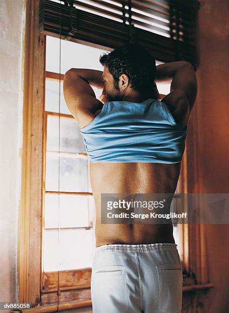 portrait of a man in front of a  window undressing - uitkleden stockfoto's en -beelden
