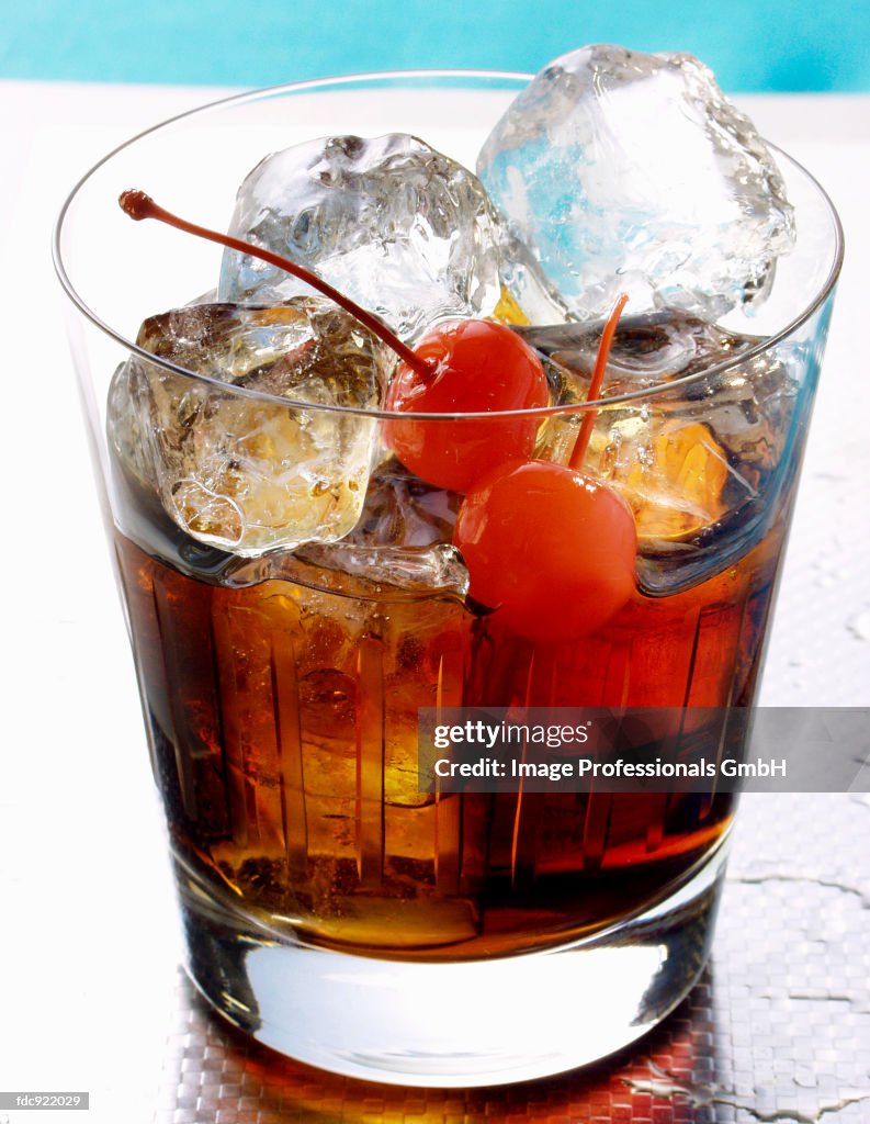Drink with rum, ice cubes and cocktail cherries