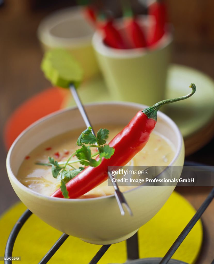 Chili pepper on fondue stick above cheese and chili sauce