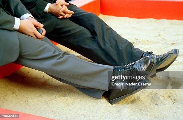two businessmen sitting in a sandbox - sandkasten stock-fotos und bilder