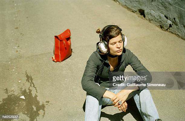 a young woman listening to headphones while sitting on pavement - simoneau stock-fotos und bilder