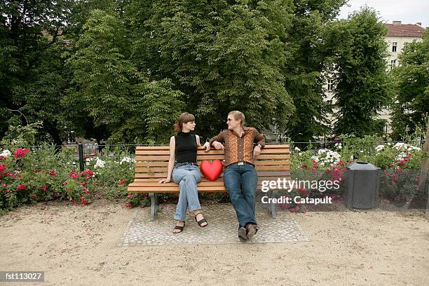 man and woman sitting on park bench with heart pillow - staring stock pictures, royalty-free photos & images