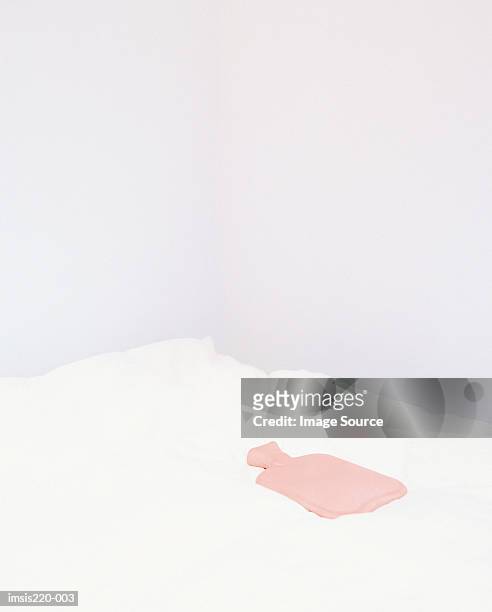 a hot-water bottle on a white bed - wärmflasche stock-fotos und bilder