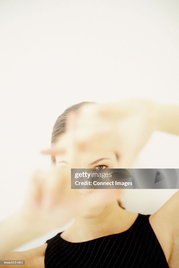 A young woman framing part of her face with hands showing her left eye