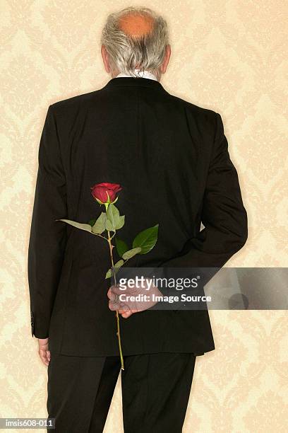 senior man hiding red rose - hands behind back stock photos et images de collection