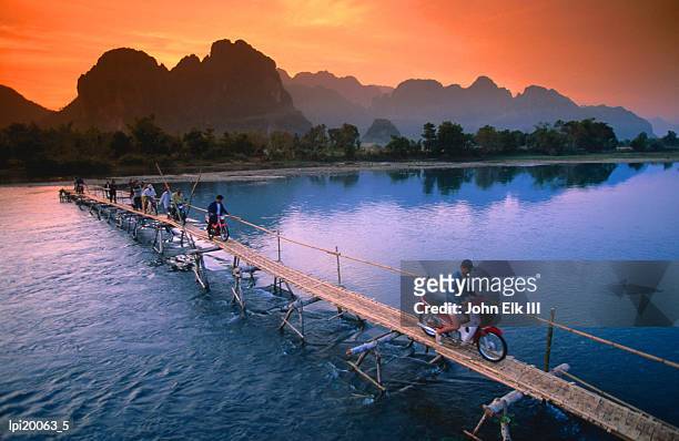 people crossing bridge across nam song river by motorbike, vang vieng, laos - laos foto e immagini stock