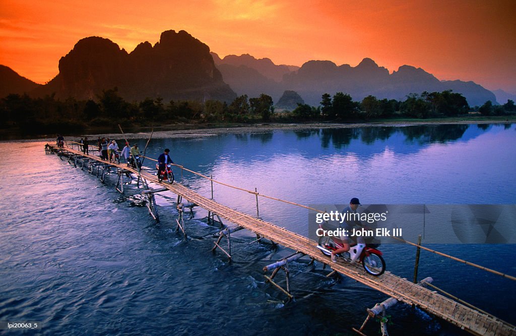 People crossing bridge across Nam Song River by motorbike, Vang Vieng, Laos