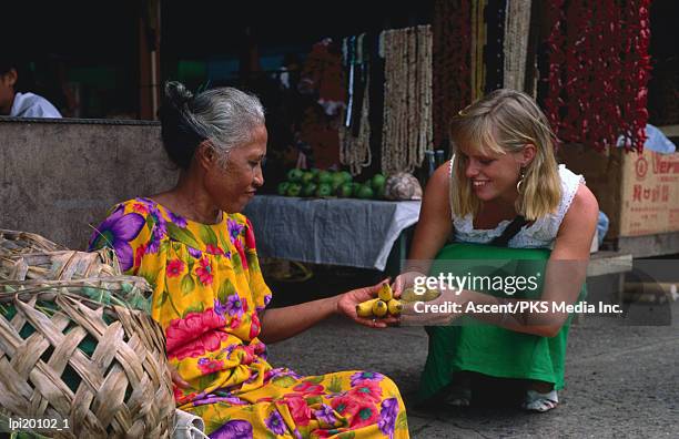 female tourist buying bananas from local woman at market, apia, samoa - apia photos et images de collection