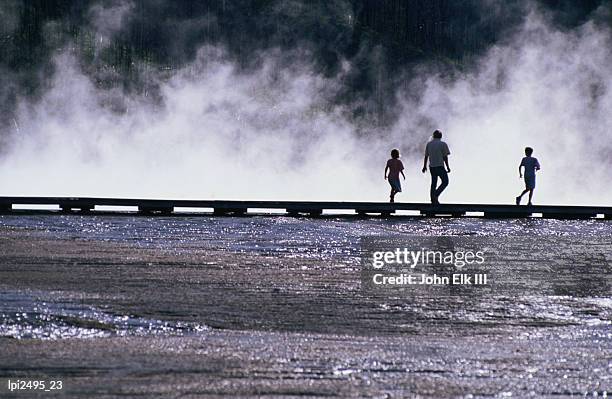 tourists silhouetted against steam from grand prismatic spring in midway basin, rear view, yellowstone national park, united states of america - midway foto e immagini stock