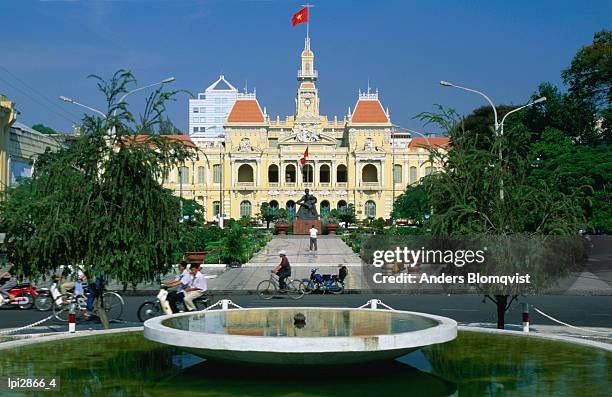 people riding bikes past fountain and town hall, ho chi minh city, ho chi minh, vietnam, south-east asia - ho stock pictures, royalty-free photos & images