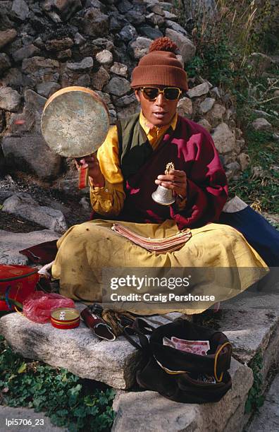 monk performing ritual in chingdrol chiling park, using hand-held drum (damaru) and bell, front view, lhasa, china - tibet autonomous region stock pictures, royalty-free photos & images