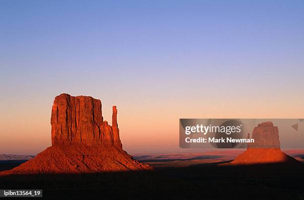 sunlight strikes the east and west mitten buttes, surrounded by barren landscape., monument valley navajo tribal park, arizona, united states of america, north america - the mittens stockfoto's en -beelden