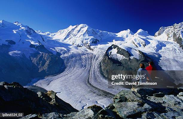 hikers on a rock at gornergrat look towards liskamm and the gorner glacier., zermatt, valais, switzerland, europe - alpes peninos fotografías e imágenes de stock