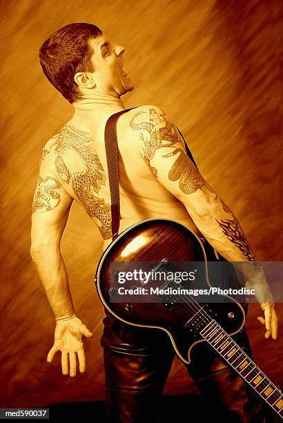 back view of bare-chested, tattooed man with guitar - modern rock stock pictures, royalty-free photos & images