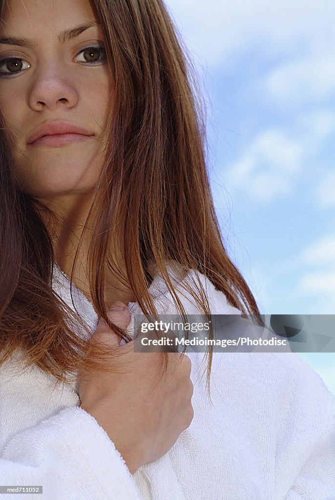 Pensive woman with hand at neck and wearing bathroom outdoors, close-up