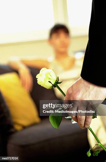 woman sitting on couch and man standing in front of her holding a single yellow rose, close-up, focus on foreground - enkele roos stockfoto's en -beelden