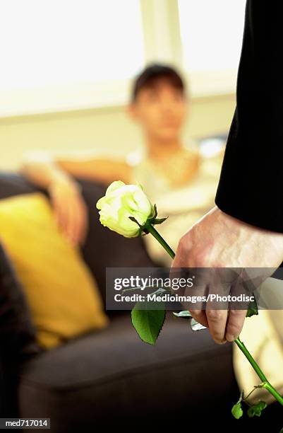 woman sitting on couch and man standing in front of her holding a single yellow rose, close-up, focus on foreground - single rose imagens e fotografias de stock