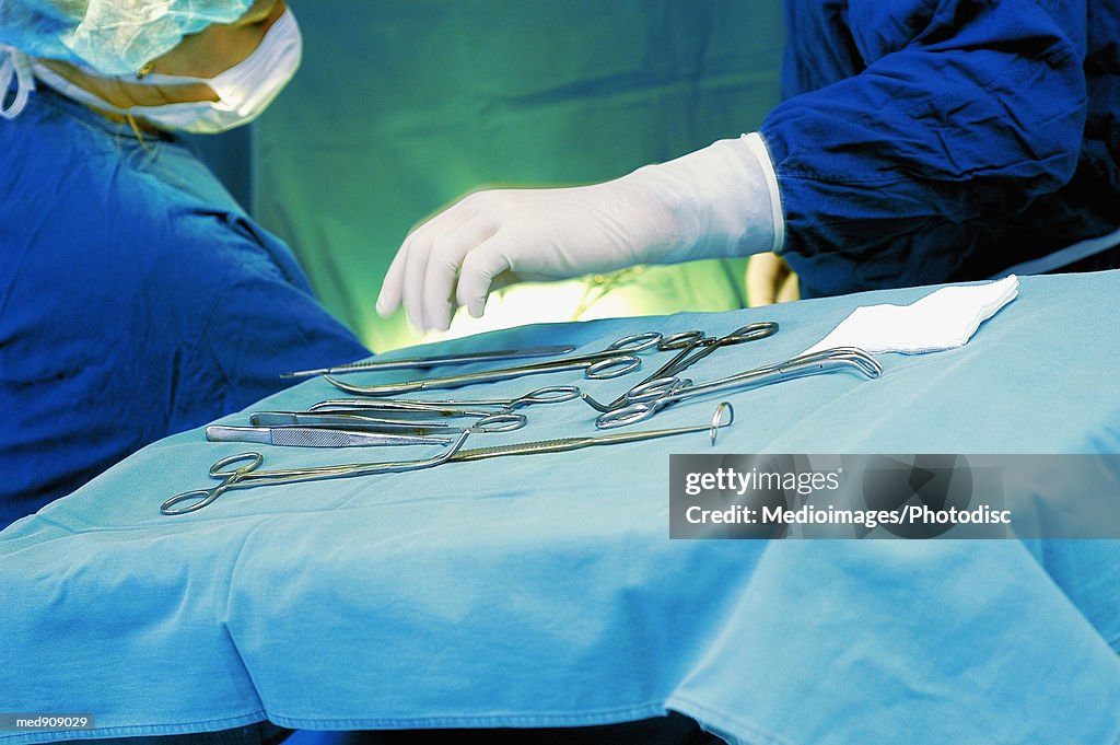 Surgeon reaching for surgical tool, with nurse assisting, close-up, part of