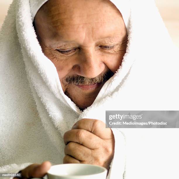 senior man with towel wrapped around head and holding a coffee cup, close-up - wrapped in a towel stock-fotos und bilder