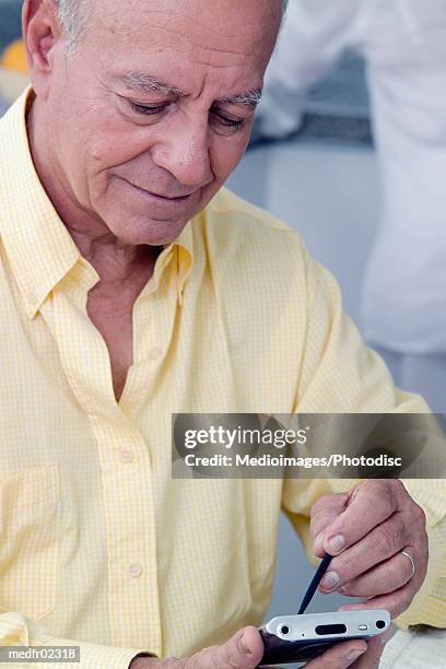 smiling senior man in yellow shirt using palmtop computer, close-up - silver surfer stock pictures, royalty-free photos & images