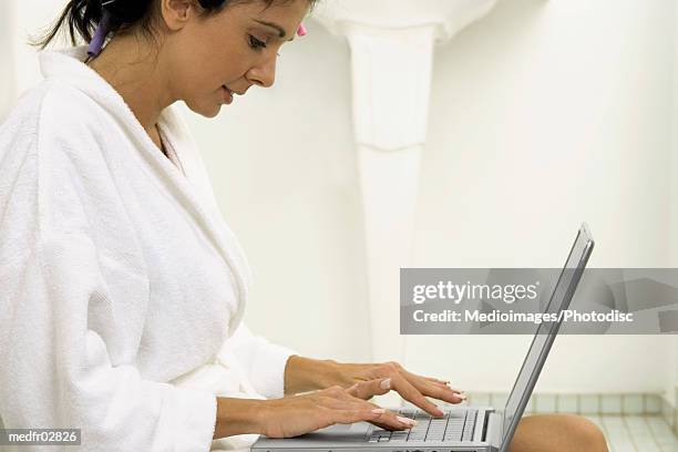 mid adult woman with curlers in hair using laptop computer in bathroom, close-up, part of - hair curlers stockfoto's en -beelden