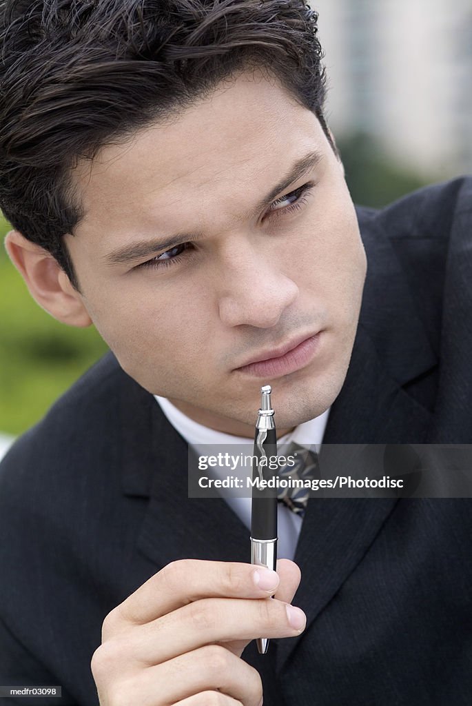 Young businessman holding pen in front of mouth, close-up
