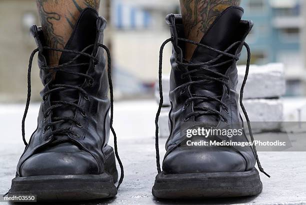 a person with tattooed legs wearing black boots - untied shoelace stock pictures, royalty-free photos & images