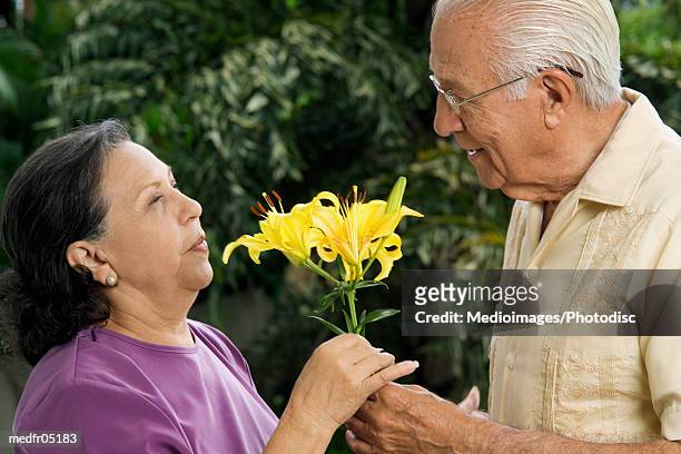senior man giving senior woman flowers outdoors, close-up - lili gentle fotografías e imágenes de stock