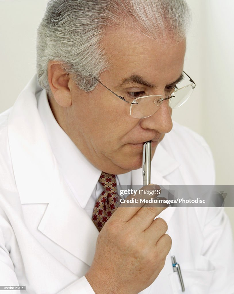 Doctor holding pen to mouth and looking down, close-up