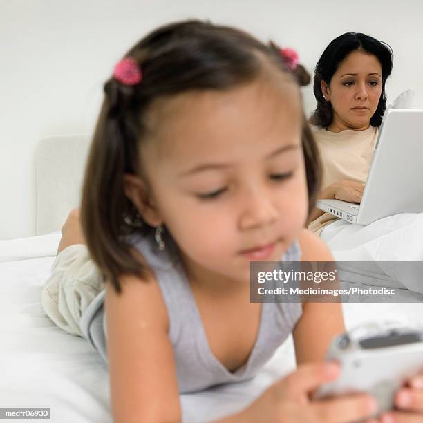 three year old girl with palmtop on bed and mother using laptop behind her, close-up - marvista entertainment parkside pictures with the cinema society host a screening of the year of spectacular men after party stockfoto's en -beelden