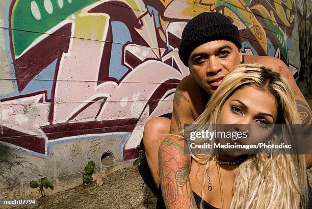 portrait of goth couple standing in front of wall with graffiti outdoors with woman in front of man, close-up - gestalt stock-fotos und bilder
