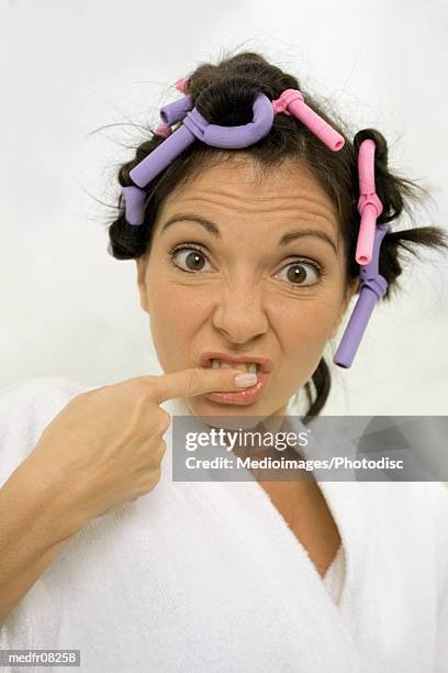 a woman with curlers in her hair brushing her teeth with her fingers - hair curlers stockfoto's en -beelden