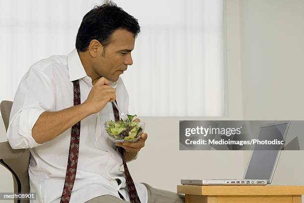 a man eating a bowl of salad and looking at a laptop - untied stock pictures, royalty-free photos & images